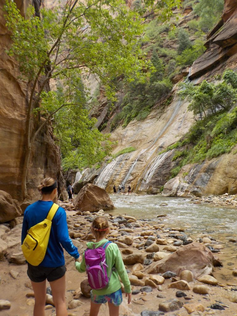 Mother and daughter hike along shore in The Narrows in Zion National Park